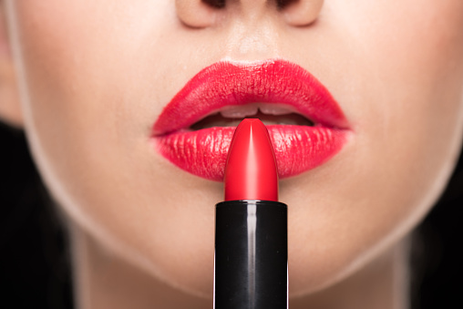 Close-up partial view of young stylish woman applying red lipstick on black