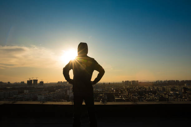 istock Young man looking city sunset,standing on top of roof 657449382
