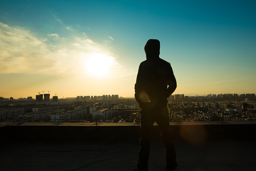 Young man looking city sunset,standing on top of roof