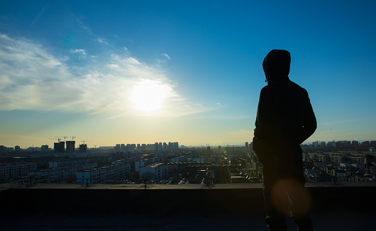 Young man looking city sunset,standing on top of roof