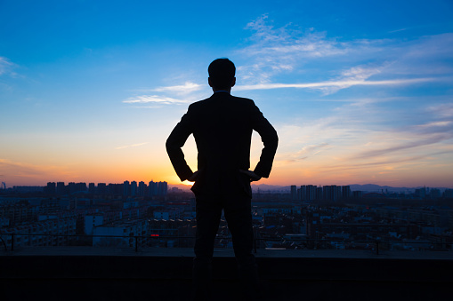 Businessman looking city sunset on top of roof