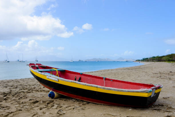 Colorful boat on a beach on the island of Saint Kitts and Nevis in the caribbean. Large yachts and sail boats can be seen in the background.  The island of Nevis is at a distance behind the mountains.