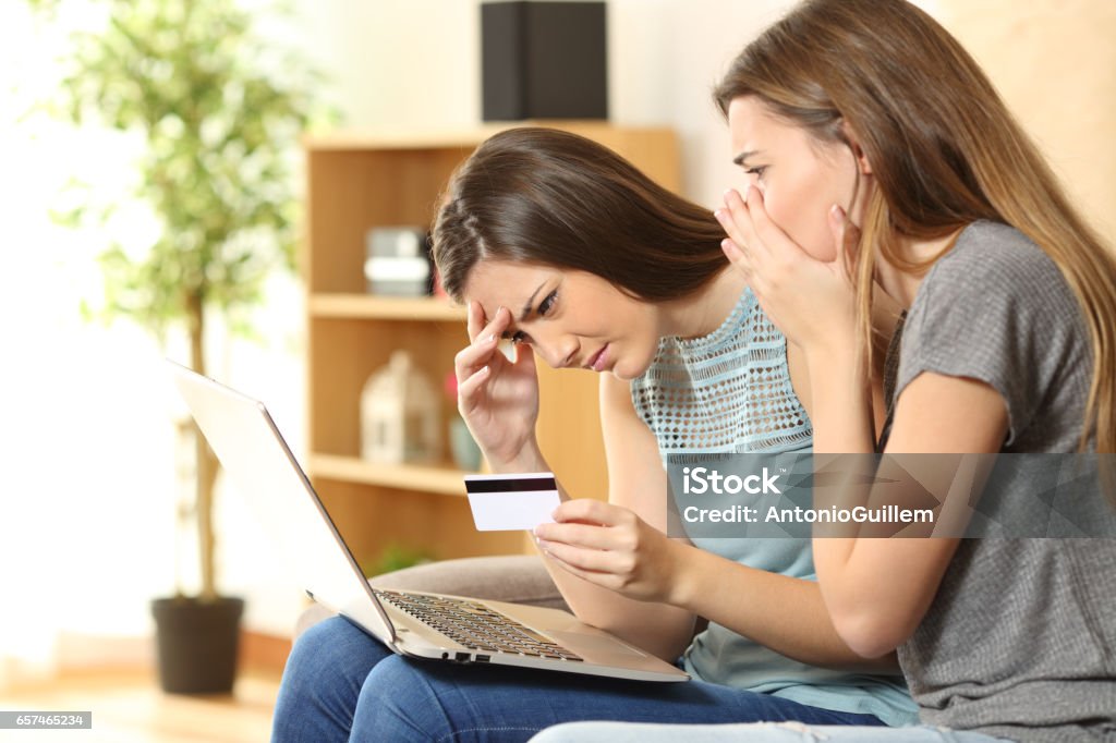 Worried roommates having problems buying online Two worried roommates having problems buying on line sitting on a couch in the living room in a house interior Identity Theft Stock Photo