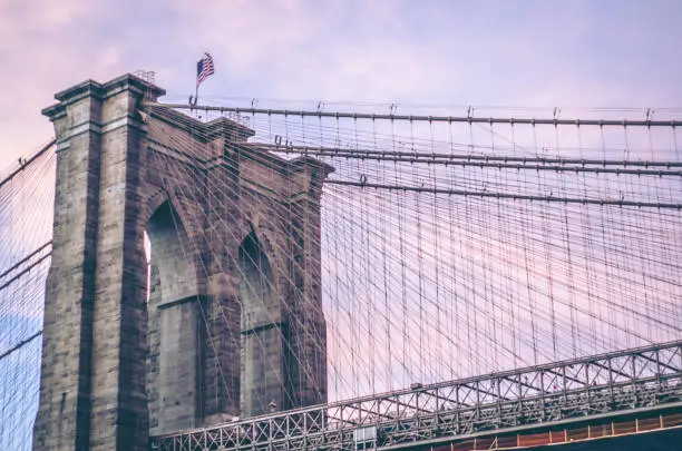 A dramatic purple sunset cloudscape and the historic Brooklyn Bridge in the foreground which connects Brooklyn New York with the Island of Manhattan. One of the most famous tourist destinations in the world and visited by millions each year.