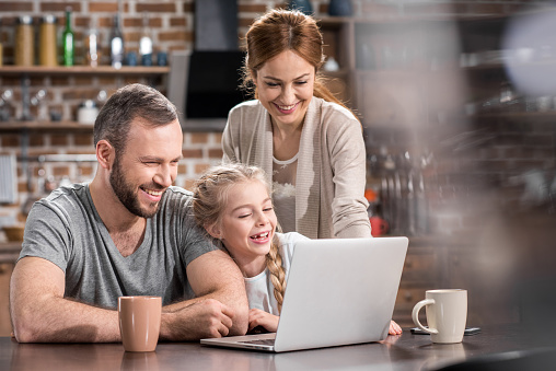 Young family using laptop in kitchen and laughing