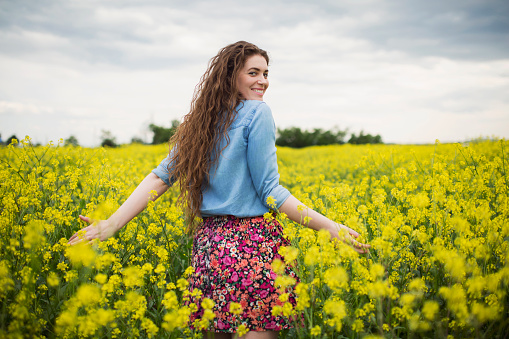 Beautiful young woman enjoying a carefree springtime day in the yellow field of wildflowers.