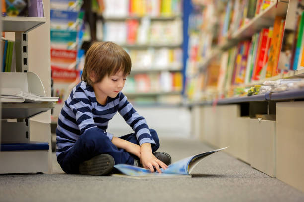 adorable niño, niño, sentado en una tienda de libros, libros de lectura - school library fotografías e imágenes de stock