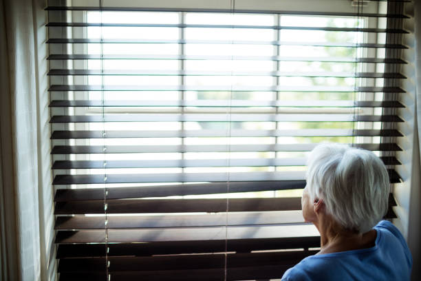 istock Senior woman looking out from window blind 657511224