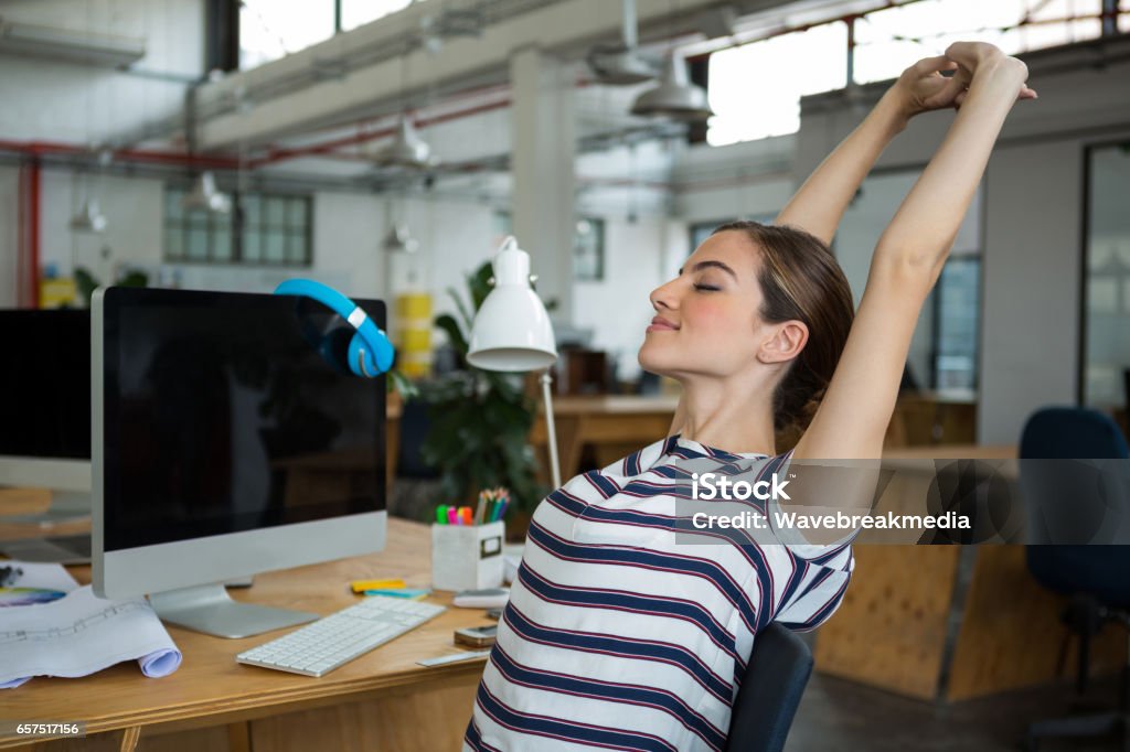 Female graphic designer sitting on chair and stretching her arms Female graphic designer sitting on chair and stretching her arms in creative office Stretching Stock Photo