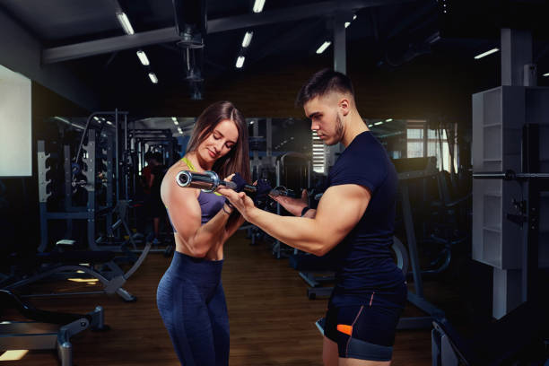 personal trainer helps a girl lifting weights in the gym - secrecy instructor exercising individuality imagens e fotografias de stock