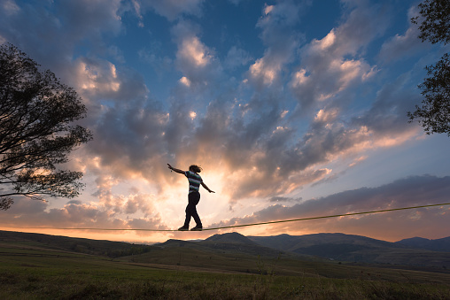 Back view of man walking on slackline tight rope in the dusk