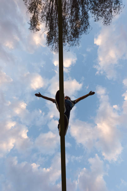 View from below of man stepping carefully on narrow slackline rope with serene blue sky in the background