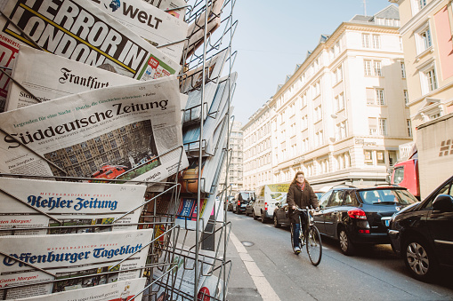 Paris: Senior cyclist woman passing near Suddeutsche Zeitung and other international magazines covers at press kiosk newsstand featuring headlines following the terrorist incident in London at the Westminster Bridge