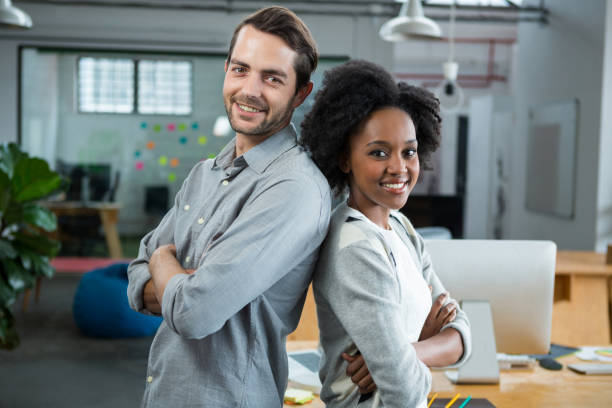 Happy man and woman standing back to back in office