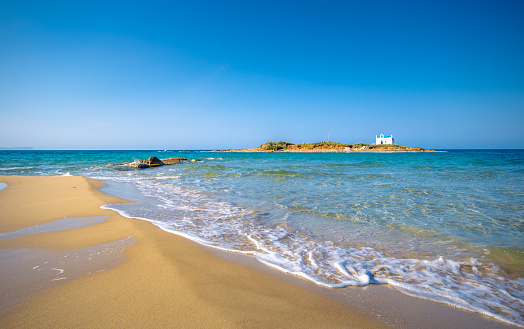 Typical summer image of an amazing pictorial view of a sandy beach with an old white church in a small island at the background, Malia, Crete, Greece.