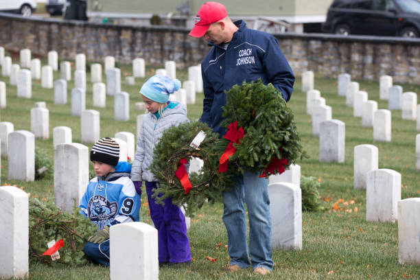 Arlington, Virginia, USA - December 17, 2016.  A family lays a wreath in front of a deceased family members greave.  Each year there is a wreath laying ceremony through the Wreaths Across America program for our nation’s veterans. Wreaths Across America is a nonprofit organization founded to continue and expand the annual wreath laying ceremony at Arlington National Cemetery.