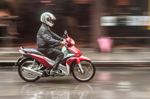 Bangkok, Thailand – May 28, 2012: A man riding a Honda motorcycle in the rain, on Sukhumvits Soi 4 in Bangkok, Thailand.