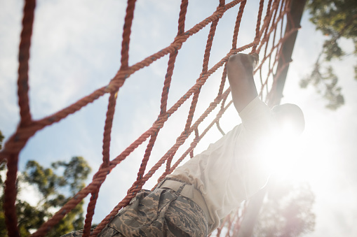 Military soldier climbing rope during obstacle course in boot camp