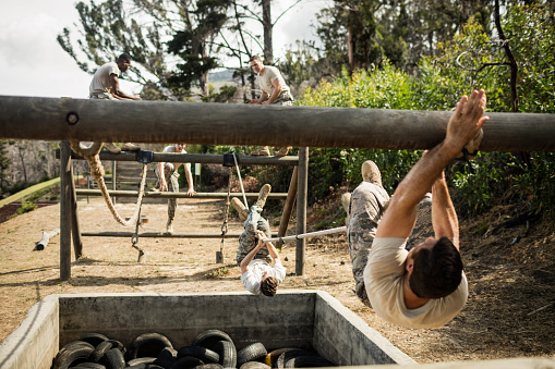 Young military soldiers practicing rope climbing during obstacle course at boot camp