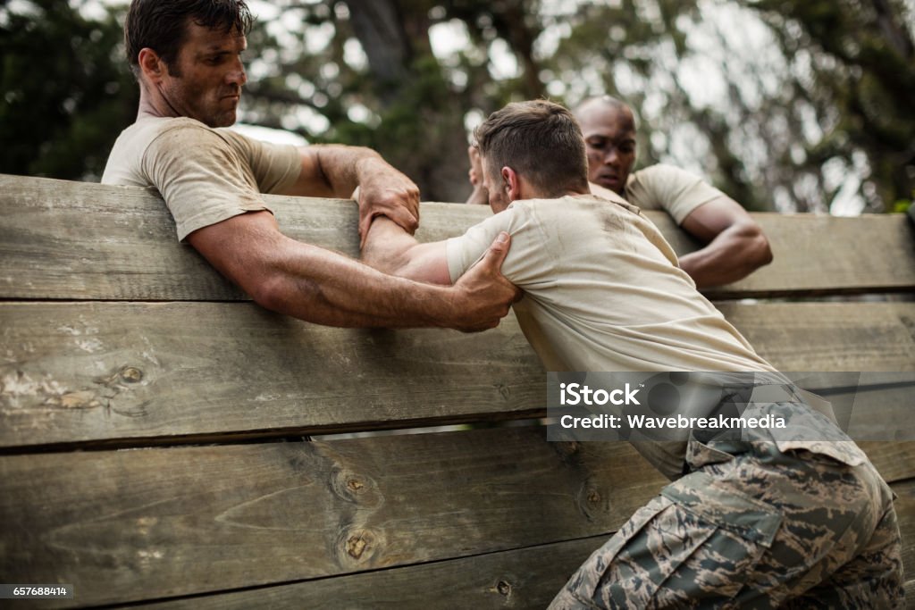 Soldiers helping man to climb wooden wall Soldiers helping man to climb wooden wall in boot camp Military Training Stock Photo