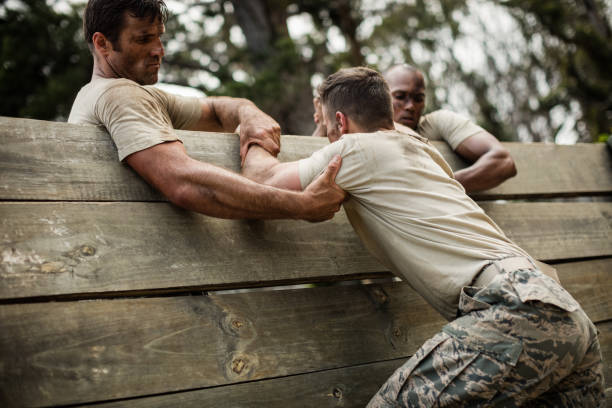 солдаты помогают человеку подняться на деревянную стену - военная подготовка стоковые фото и изображения