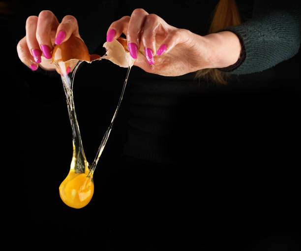 istock Yolk dropping from cracked raw egg divided by woman hands. 657733808