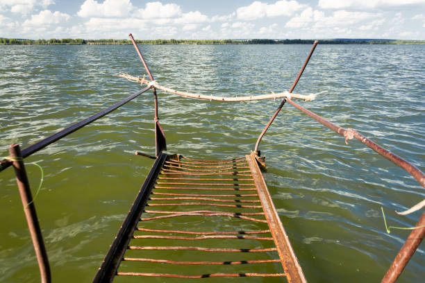 Old rusty metal footbridge on the lake. Sunny day, blue sky and green water.