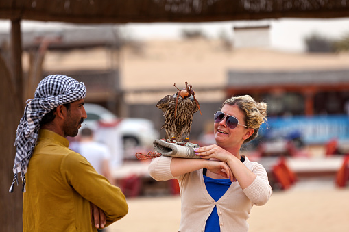 Dubai, UAE - March 22 2014: Tourist with a falcon on her right forearm and the falconer by her side in the Liwa desert just outside Dubai.