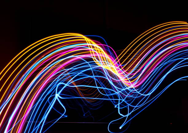 A long exposure photo of multi-colored fairy lights, dancing around. Yellow, pink and blue lights, set against a clean black background