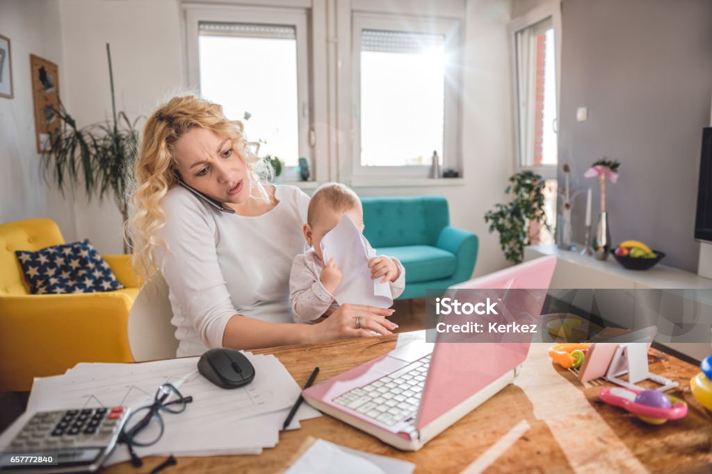 Mother talking on smart phone at home office Worried mother holding baby and talking on smart phone at home office Mother Stock Photo