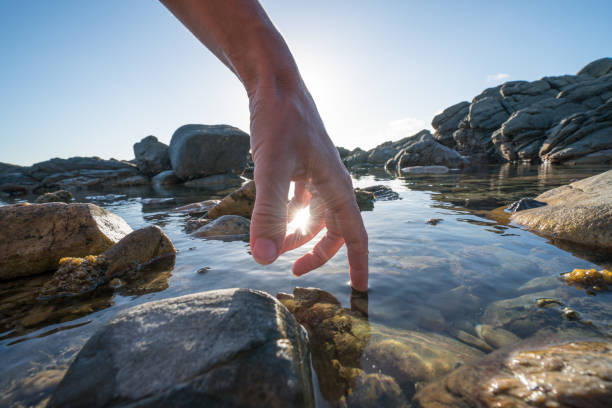 Detail of female's finger touching the surface of the sea. beautiful sunbeam and rocks.