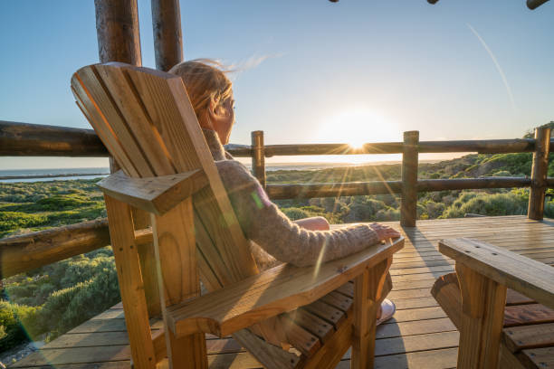 Young woman relaxing on terrace at sunset Young woman relaxing on the terrace of her wooden lodge at sunset. Idyllic setting by the sea, shot in the Southern Tip of Africa, Cape Agulhas. cottage life stock pictures, royalty-free photos & images