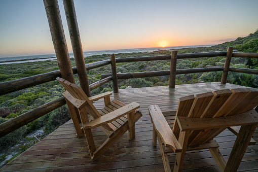 View of log cabin the nature at sunset. Wooden terrace lying on bush, sea view.