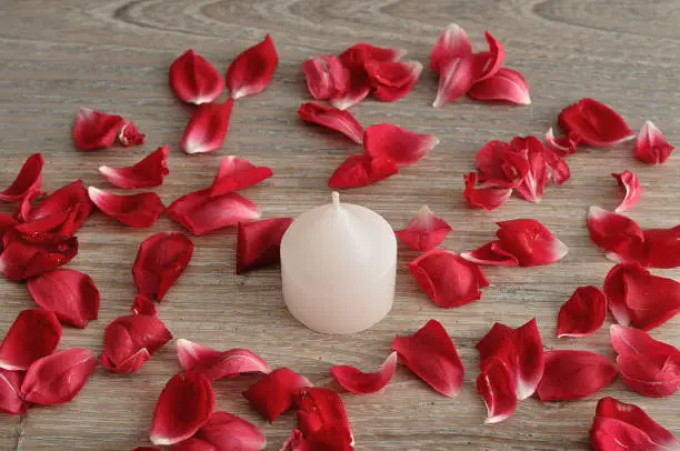 A white candle with red rose petals