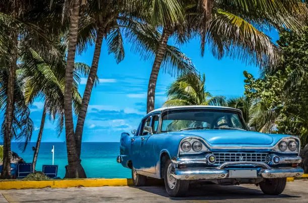 Photo of American blue vintage car parked under palms in Varadero Cuba
