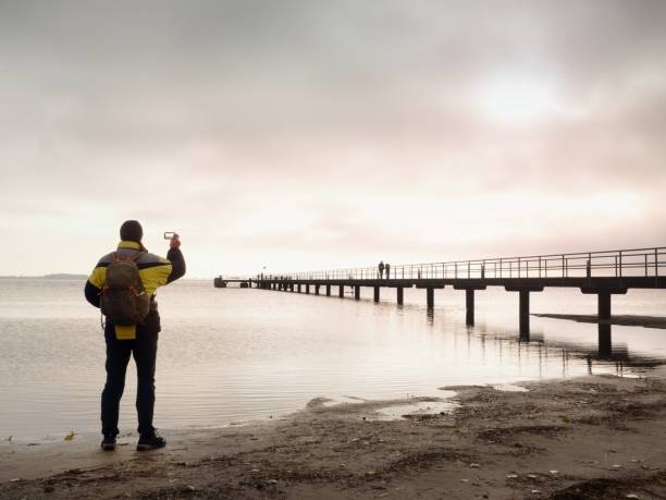 istock Hiker with backpack alone on sandy beach, sunrise above sea bridge. 657805182