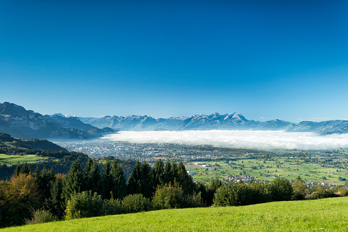 View from above to the Rhine valley in Vorarlberg, Austria at the border to Switzerland. It’s fall and there is some fog in front of the Swiss mountains.