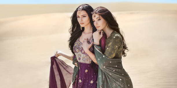 Women in desert landscape. Travel concept Travel concept. Adventure of two sisters princesses happy standing in the desert and looking at landscape. Two beautiful mixed race asian caucasianl girls enjoy a joint journey. Creative art fashion portrait shot of two gorgeous attractive models outdoors in arabian indian dresses. Copy space background on sand dunes. arabian girl stock pictures, royalty-free photos & images