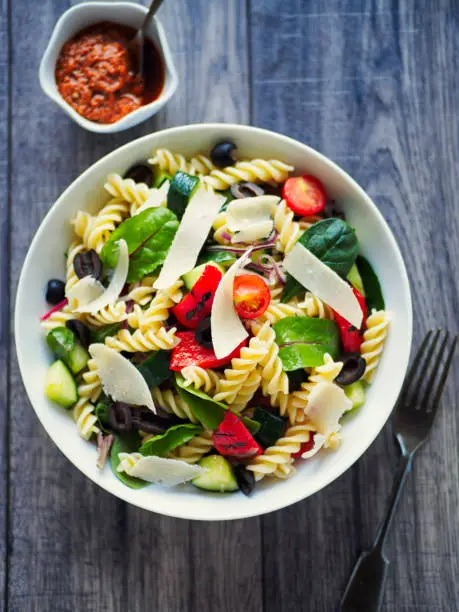Home made healthy pasta salad,mix cooked pasta with cucumber,cherry tomatoes,freshness leaves and black olives,grilled red pepper.service with red pesto sauce and shaved parmesan cheese