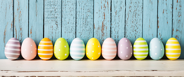 Photography of multi colored easter eggsake on a white shelf and blue old wood.