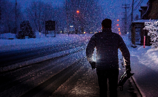 A man walks down a snowy road during a snowstorm in a village. Saint-Hugues, Quebec.