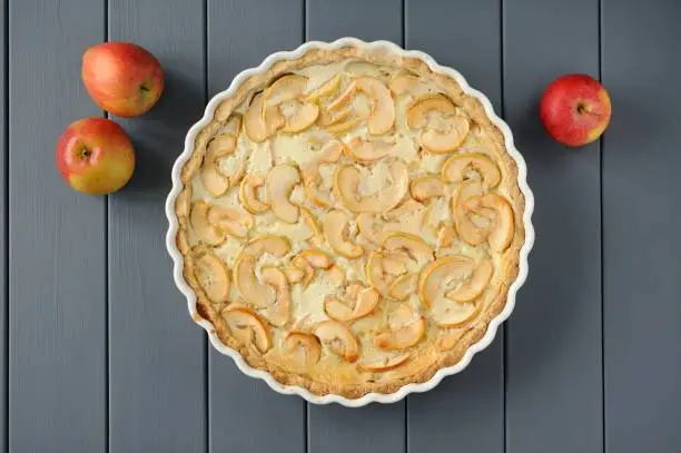 Apple tart with whole apples on grey stripped background overhead view