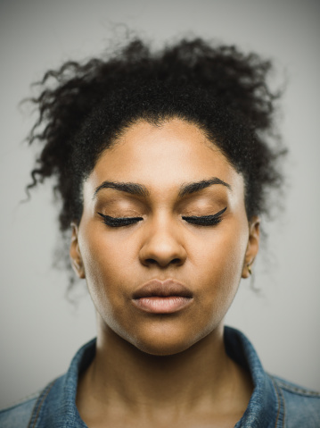 Close-up portrait of confident real young afro american woman. Beautiful female is against gray background. She is with curly black afro hair and closed eyes. Vertical studio photography from a DSLR camera. Sharp focus on eyes.