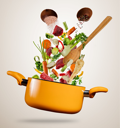 Fresh vegetable and pieces of beef meat flying into a pot with wooden spoon, separated on gray background