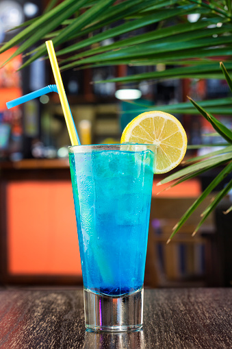 Blue lagoon cocktail in a glass with drinking straw and slice of lemon