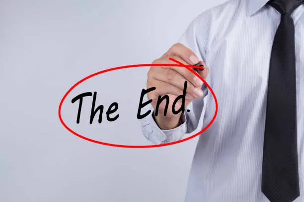 Photo of Businessman Hand Writing The end. with a marker over transparent board,  Business concept.