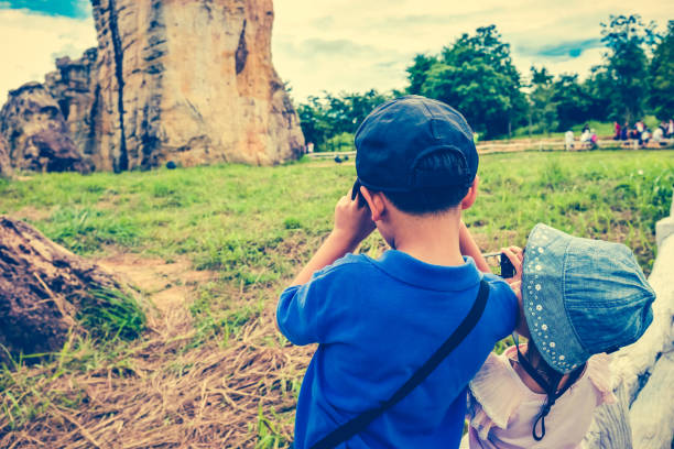 Back view of asian children taking photos by camera at national park . Family relaxing outdoors with bright sunlight on summer day, travel on vacation. Child in nature. Cross process and vintage tone.