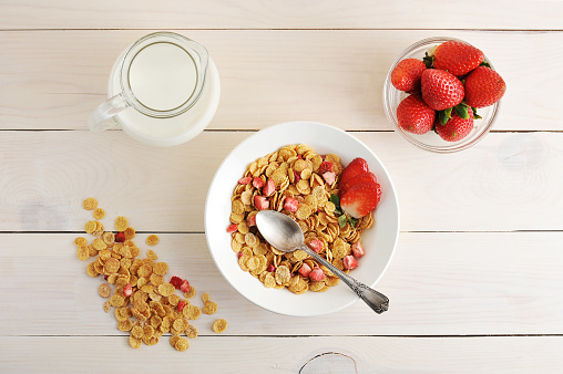 cornflakes with strawberries and milk - a healthy Breakfast on a white wooden background - top view