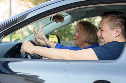 Motor accident about to happen with a frantic elderly woman gesturing with her hands while the young man driving clenches his teeth and grimaces in anticipation of a crash