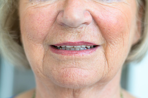 Lower face of a senior woman with wrinkled skin with her lips slightly ajar showing the tips of her teeth in a close up view